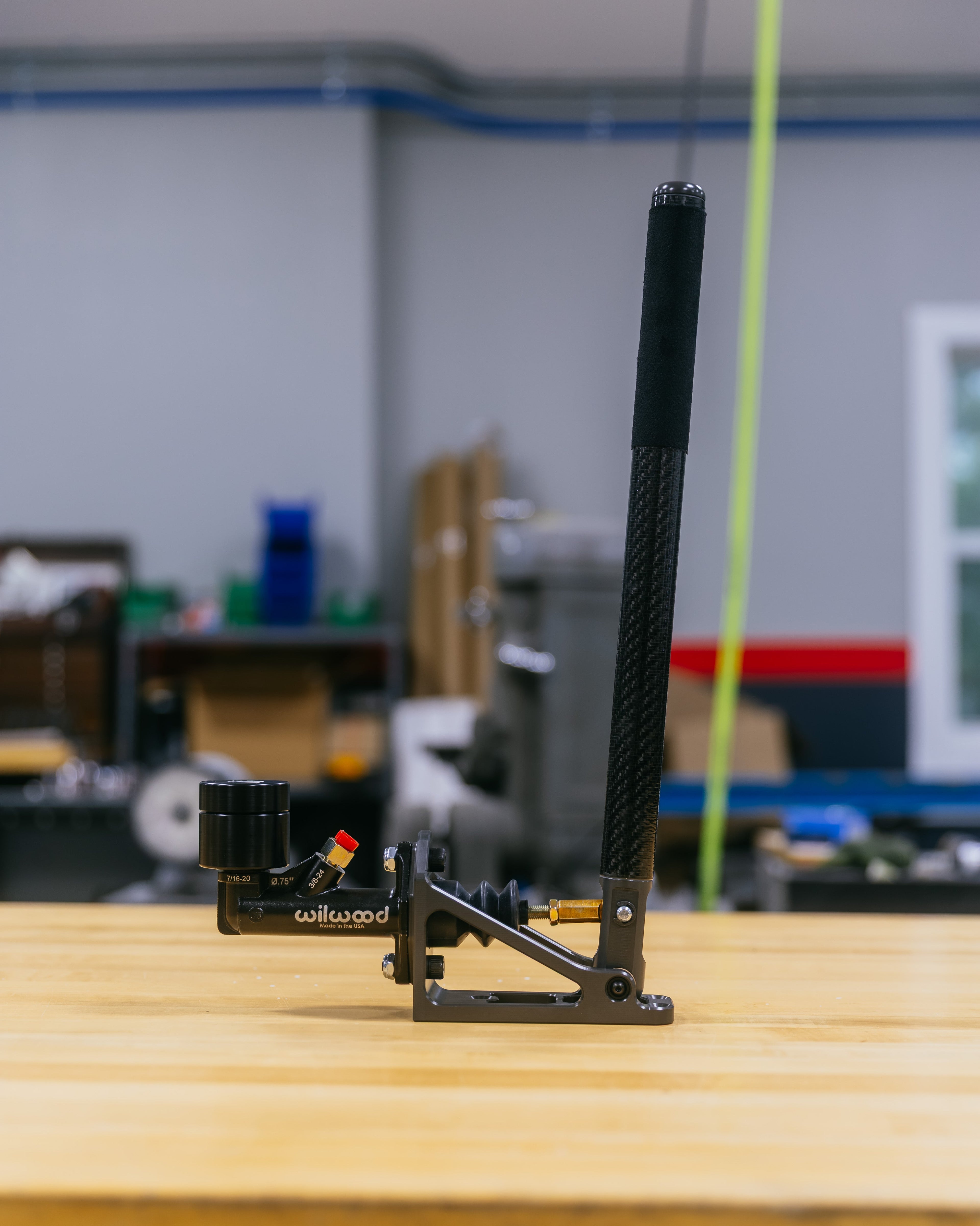 Hydraulic handbrake with carbon fiber arm on a wooden surface in a workshop setting