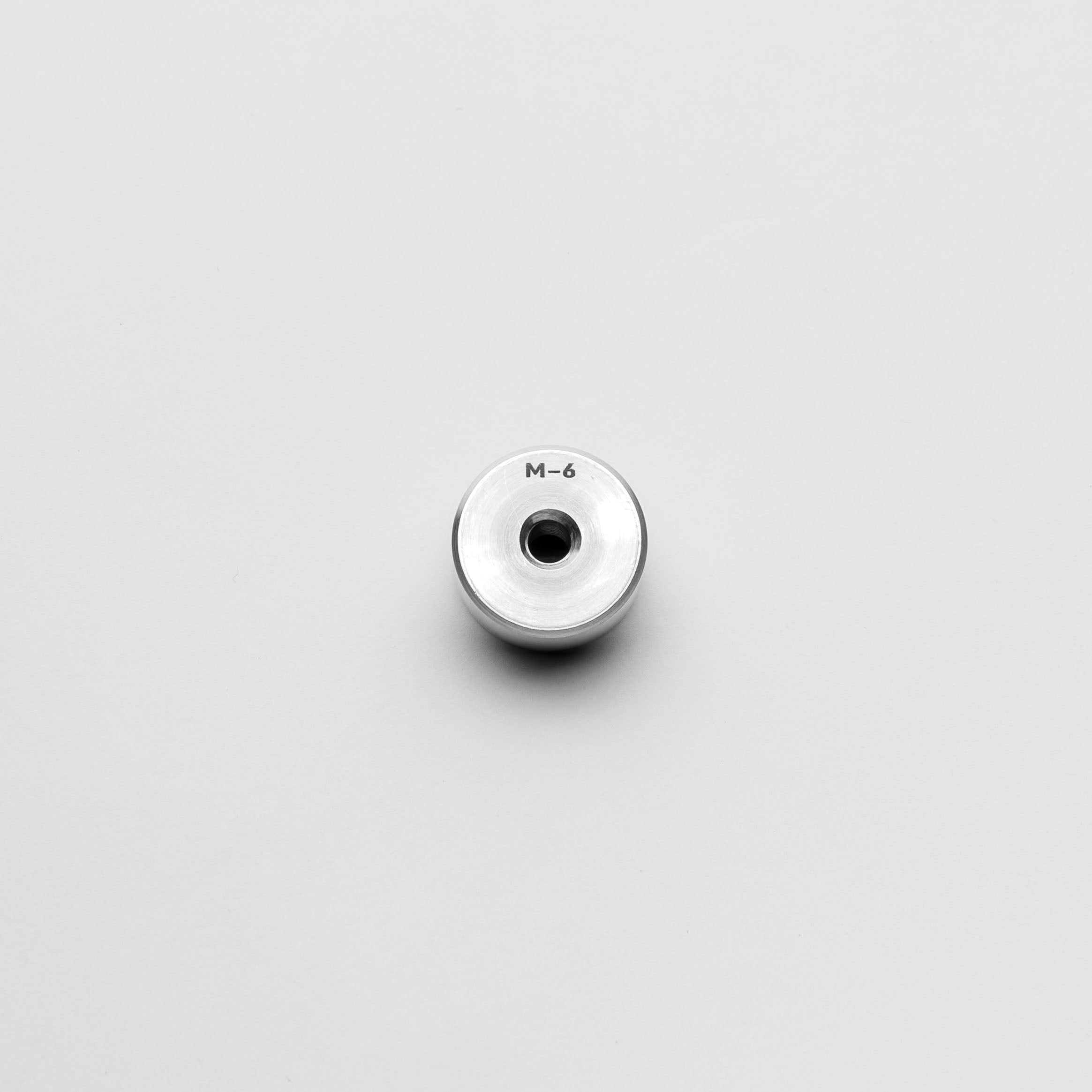 Metallic button with 'M-6' marking on a light gray background